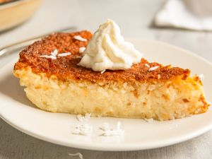 A slice of pie topped with whipped cream on a plate showing a golden crust and a moist interior