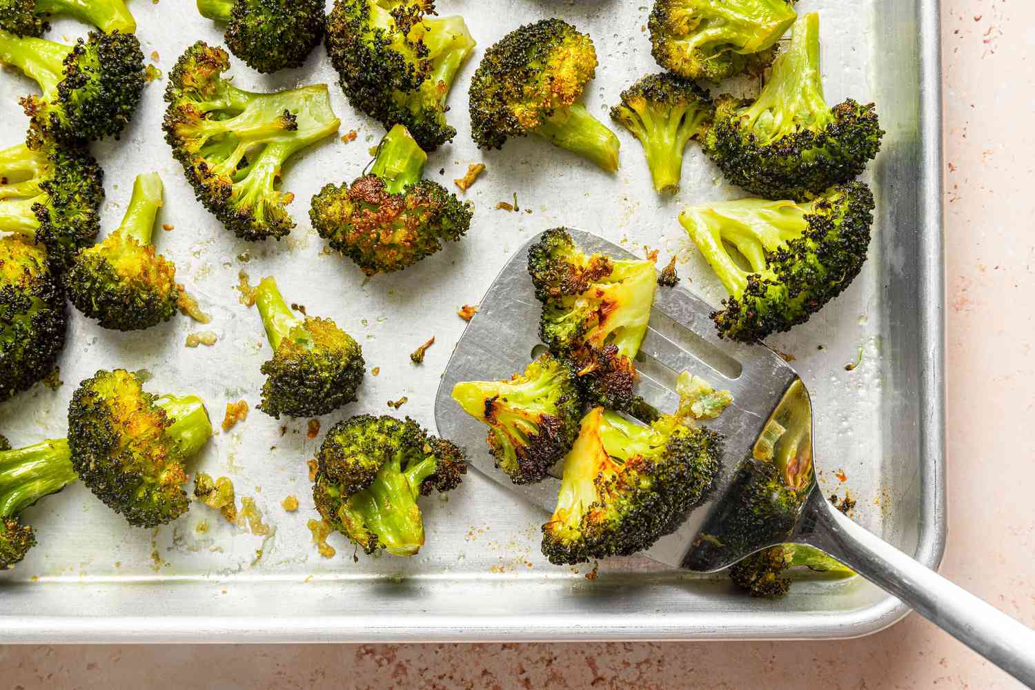 Browned broccoli florets on a sheet pan showing a metal spatula lifting up a few of the florets