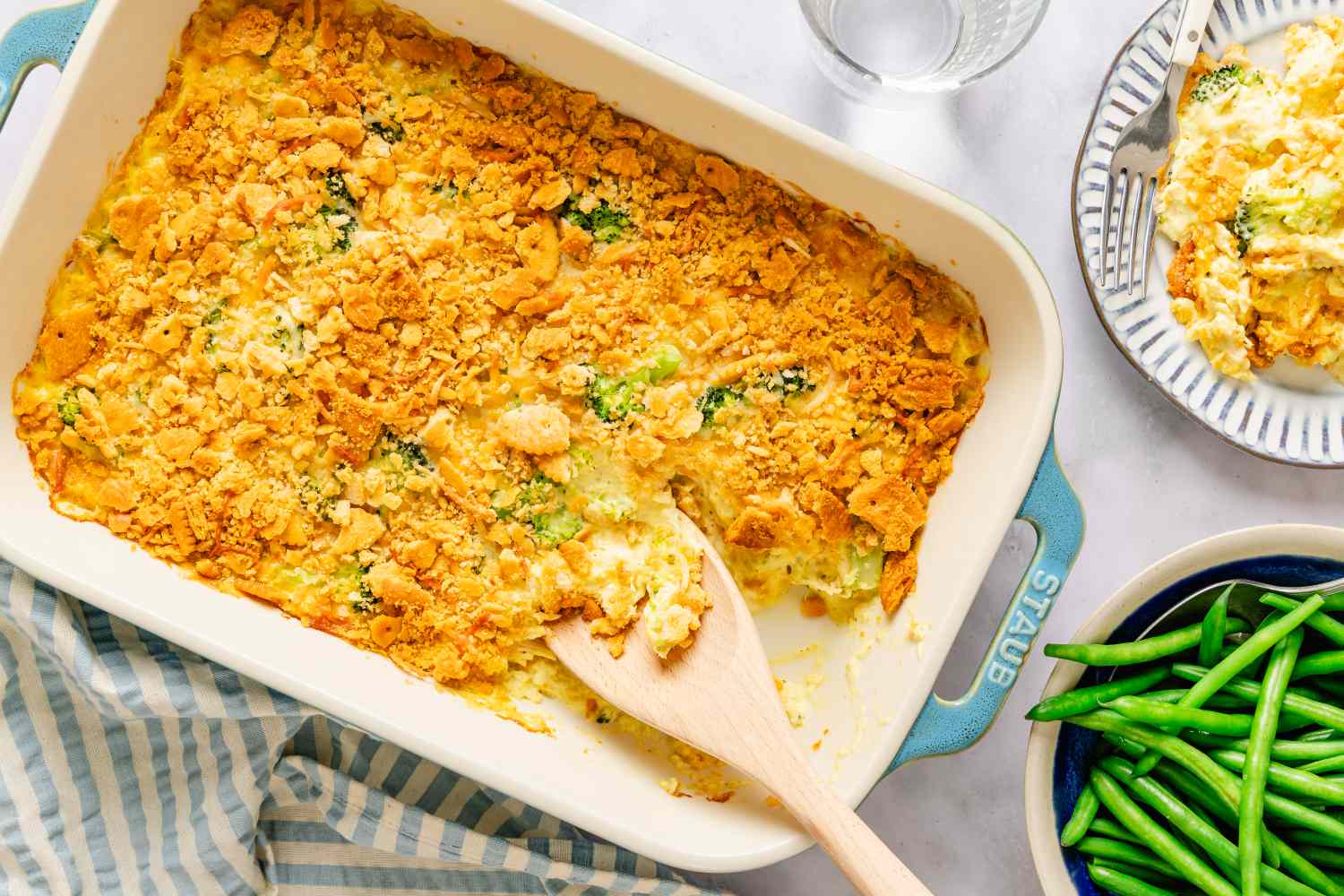 Casserole dish containing chicken divan accompanied by a plate of green beans