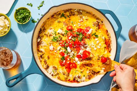 overhead view of Queso Fundido in a skillet, hand pulling dipped chip from it
