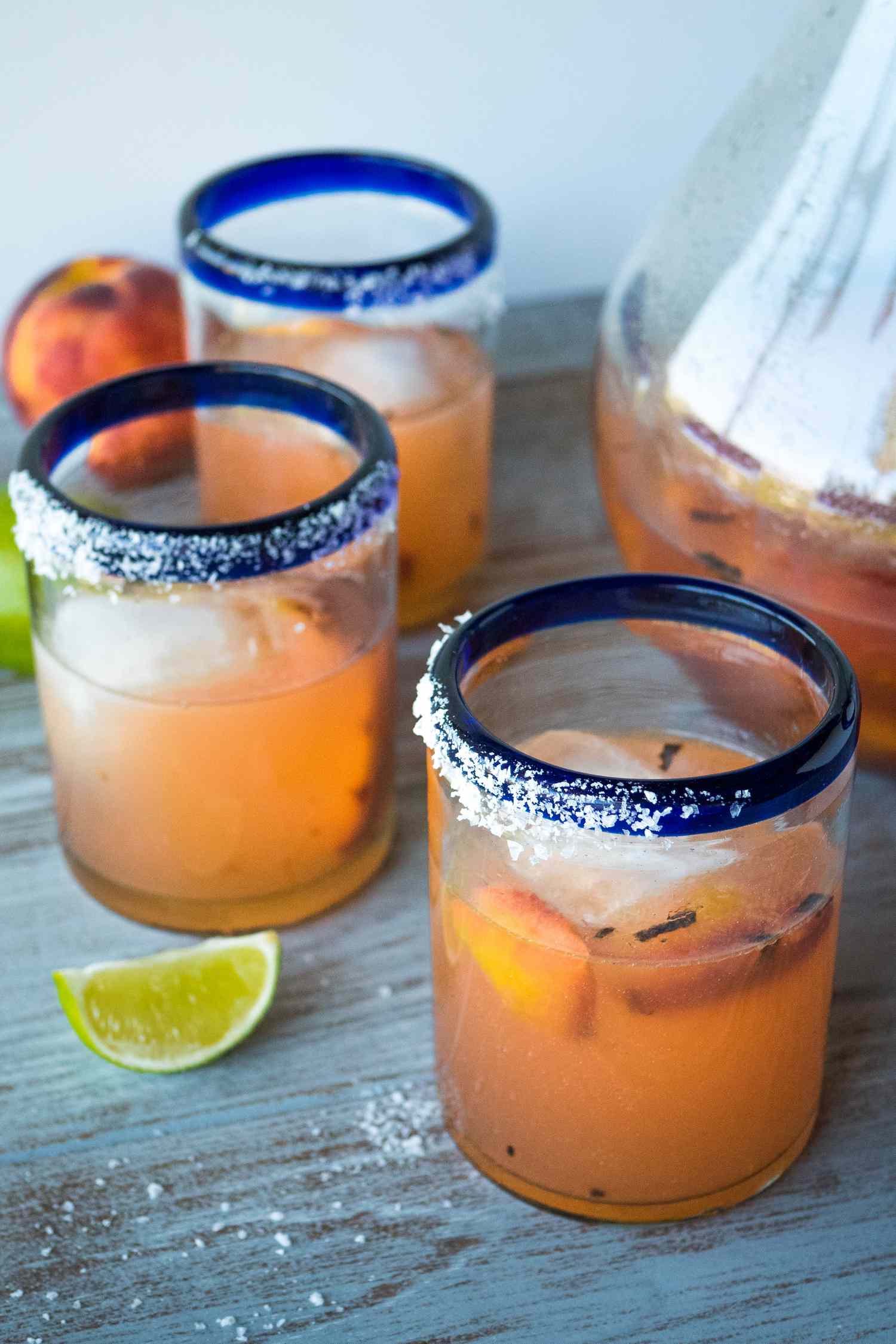 Three grilled peach pitcher margaritas on a table with limes and a pitcher.