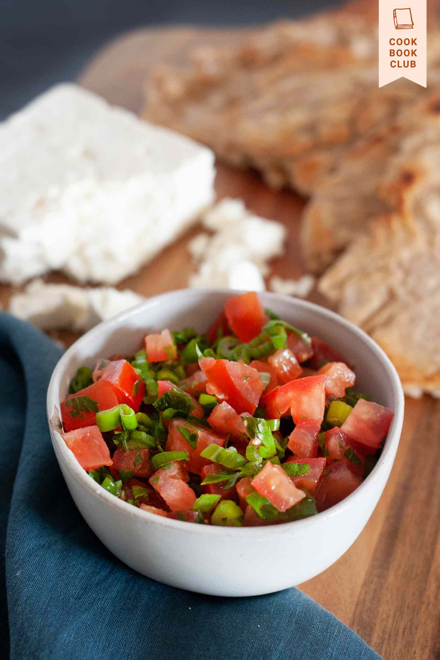 Side view of Lasary Legioma (Tomato Relish) in a white bowl set on a wooden board.