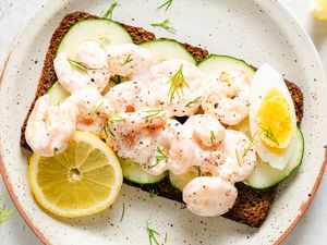 Scandinavian Shrimp Sandwich on a plate, garnished with wedge of a boiled egg, chopped fresh dill, and a lemon slice