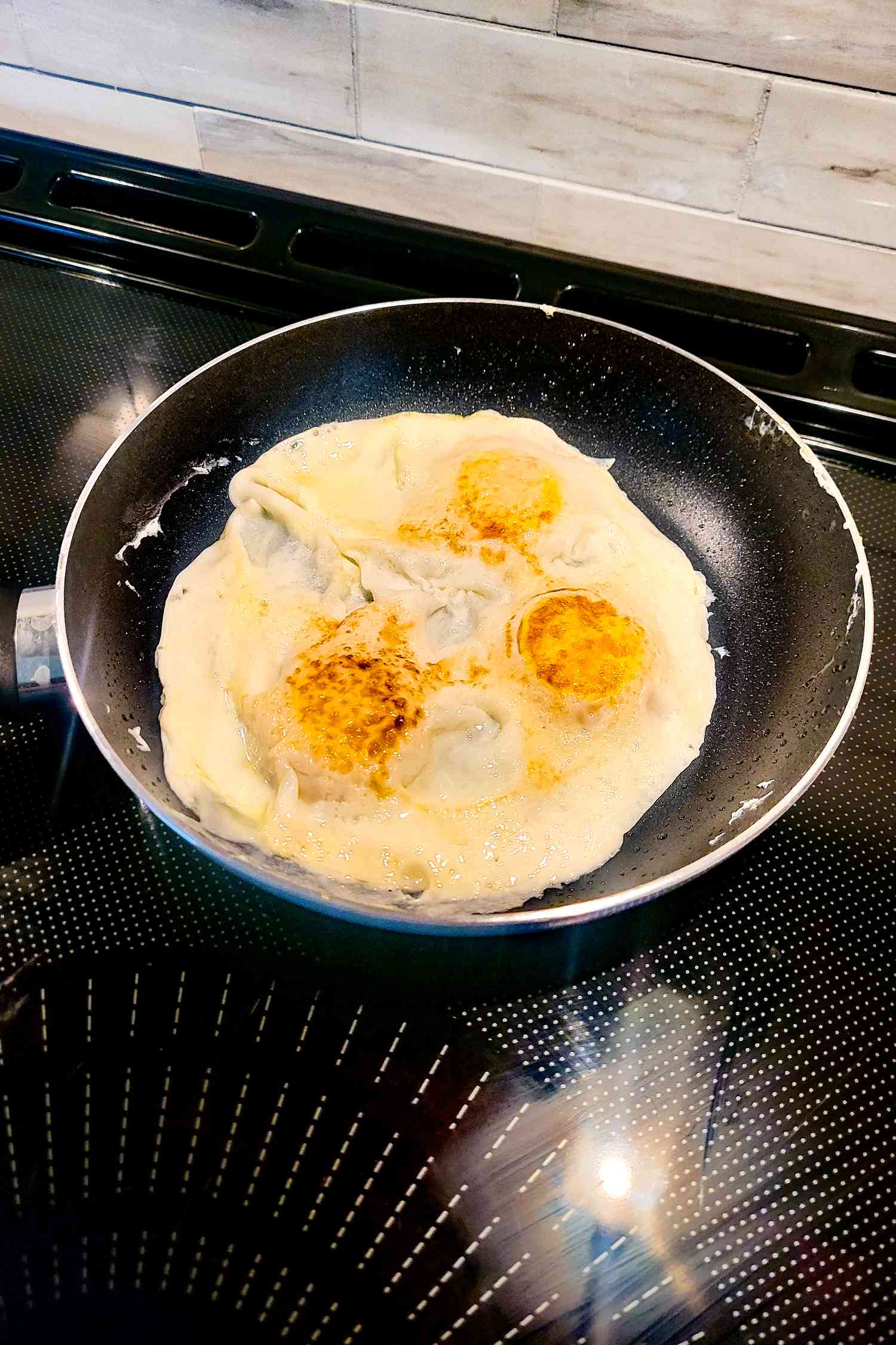 A nonstick skillet with three over-easy eggs cooking inside