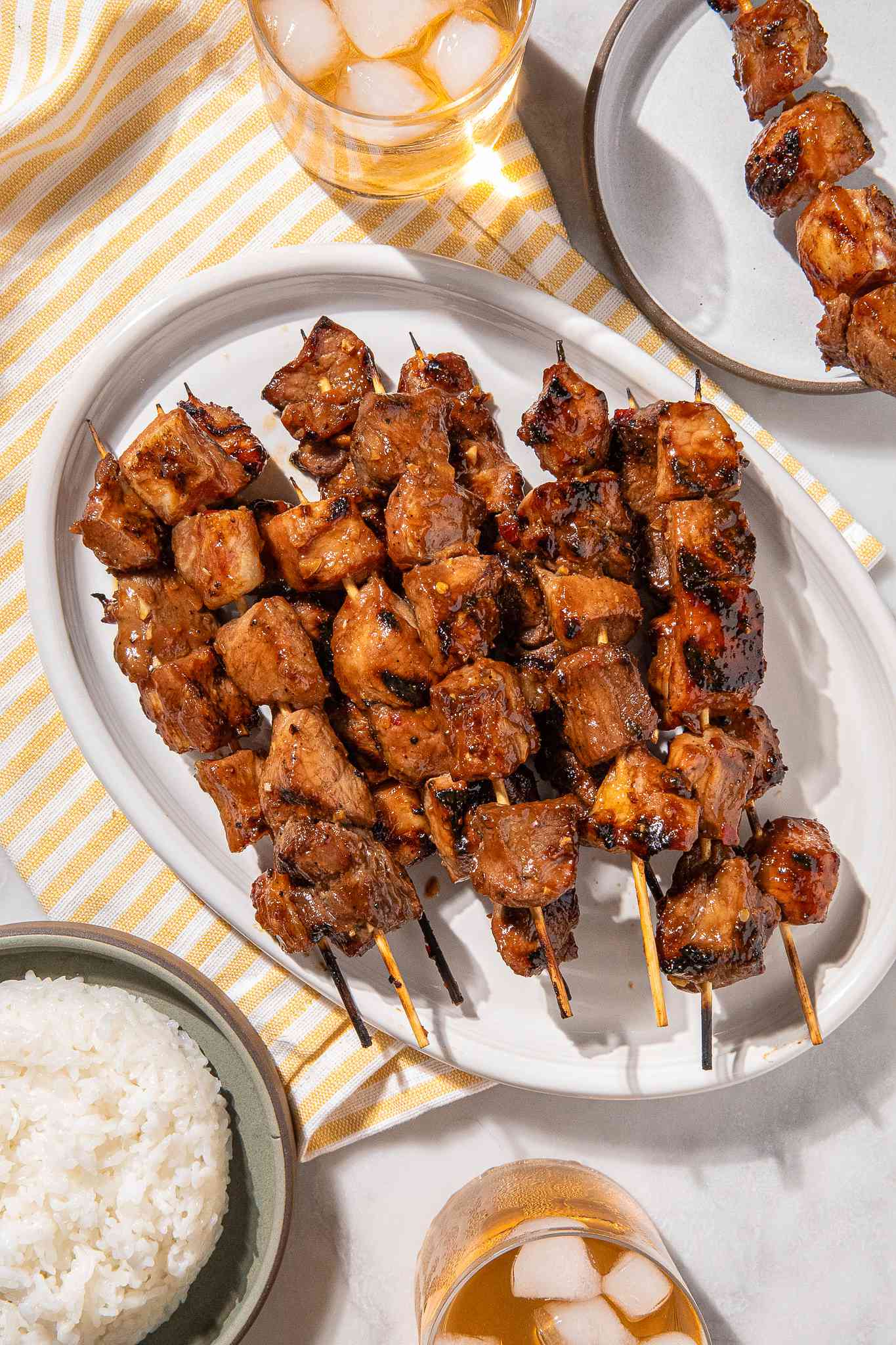 Grilled pork skewers on a white platter with rice on the side
