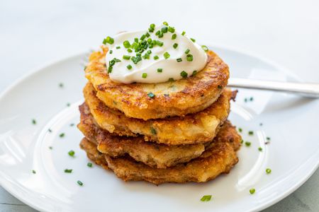 Leftover mashed potato pancakes stacked on a plate and topped with sour cream and chives.