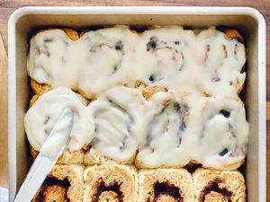 A pan of easy gluten free cinnamon rolls being topped with icing.