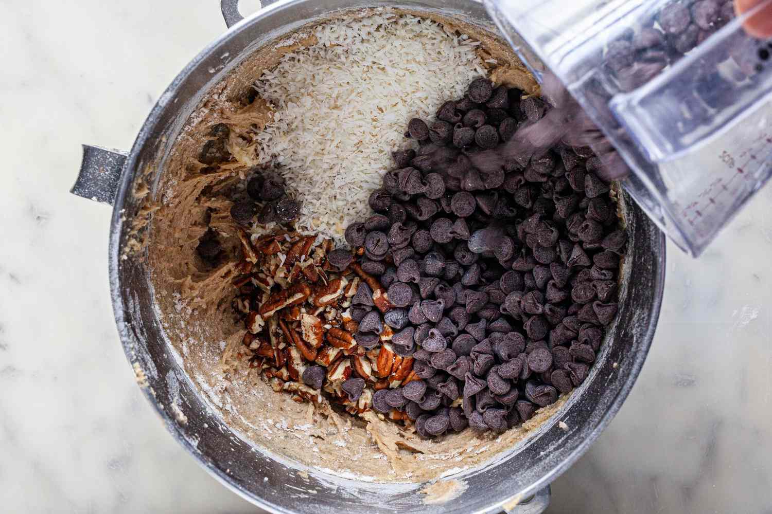 Chocolate chips, nuts, oats, and coconut added to a bowl of cookie dough to make cowboy cookies