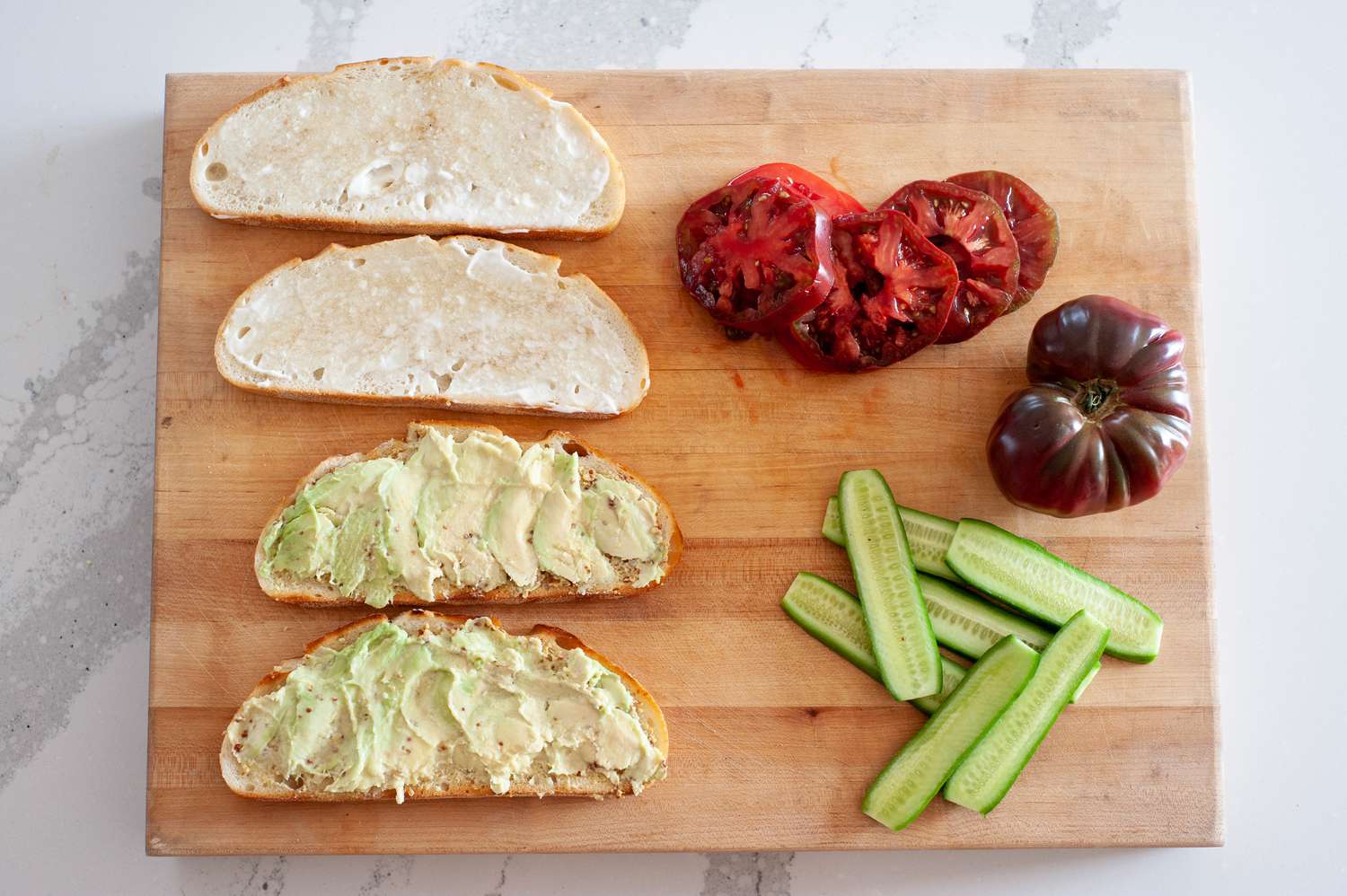 On a Cutting Board, Slices of Cucumber, Slices of Heirloom Tomato, Two Slices of Bread with Mayo, and Two with Smashed Avocado for Loaded Veggie Sandwiches Recipe