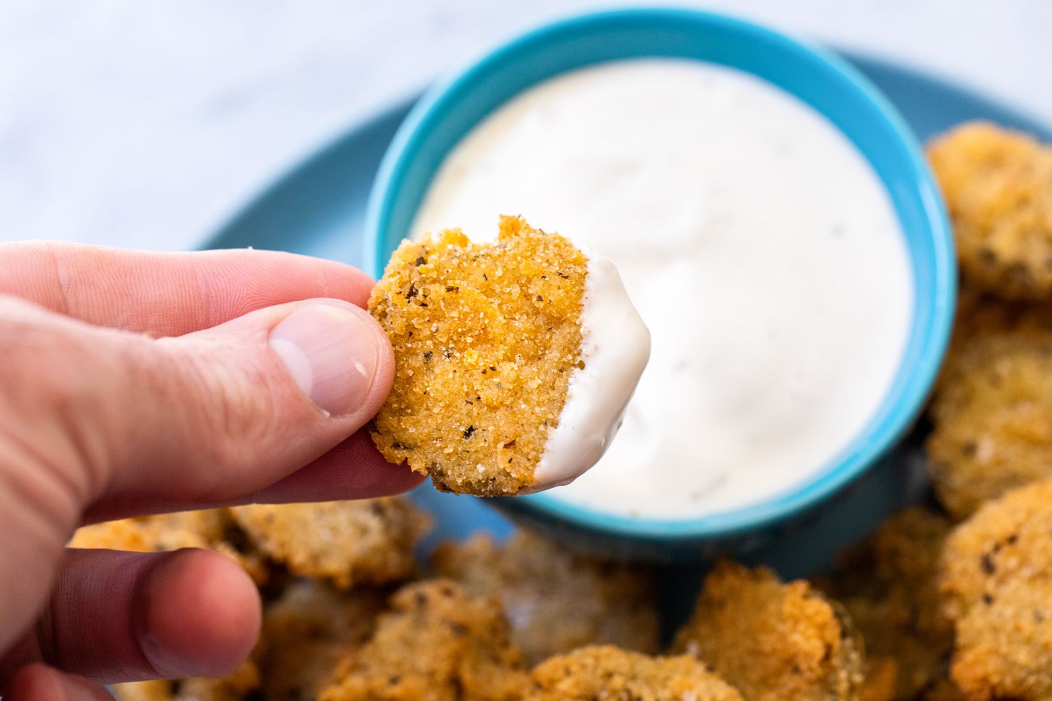 Fried Pickle Dipped into a Bowl of Dipping (on a Plate with More Fried Pickles)