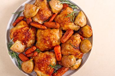 Roasted chicken thighs served with potatoes and carrots on a plate garnished with herbs
