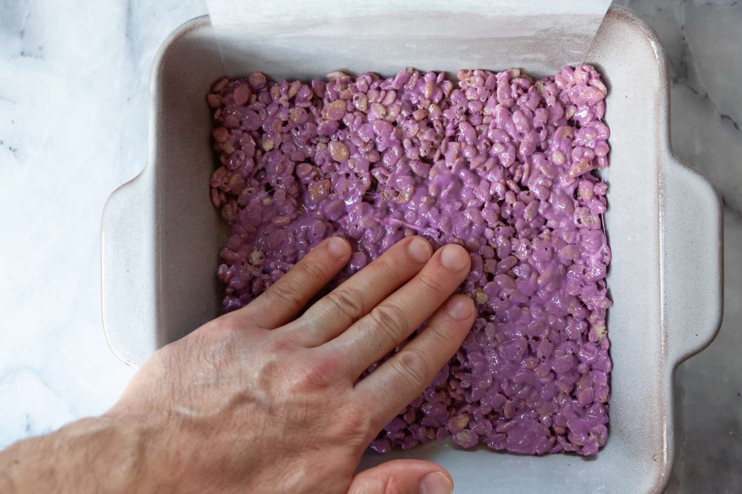 Press Down Rice Krispies and Marshmallow in Baking Pan for Rainbow Treats Recipe