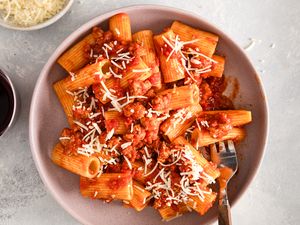 Rigatoni pasta topped with sausage tomato sauce and shredded cheese served on a plate with a fork