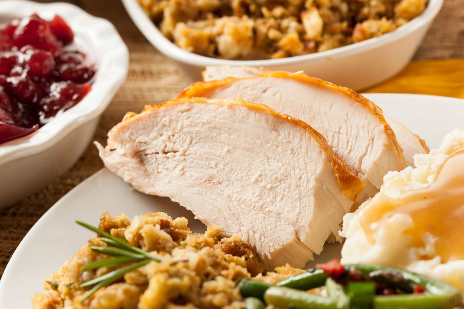 A closeup of a Thanksgiving dinner plate with sliced roast turkey, stuffing, mashed potatoes and green beans