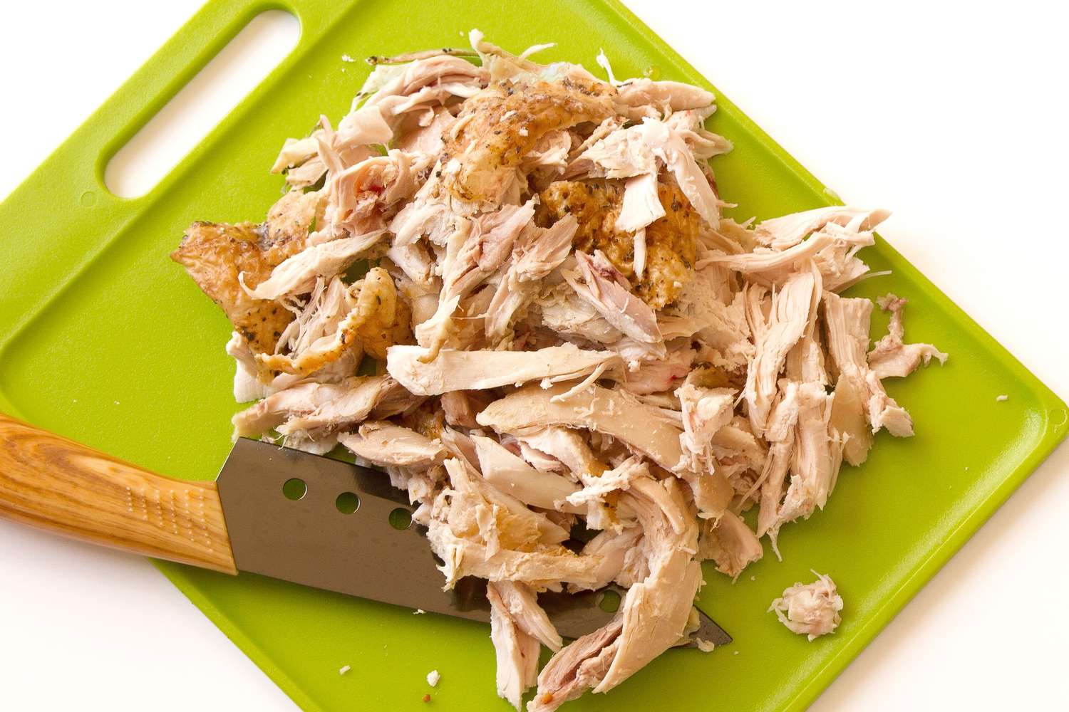 A cutting board with shredded chicken breast and a small knife