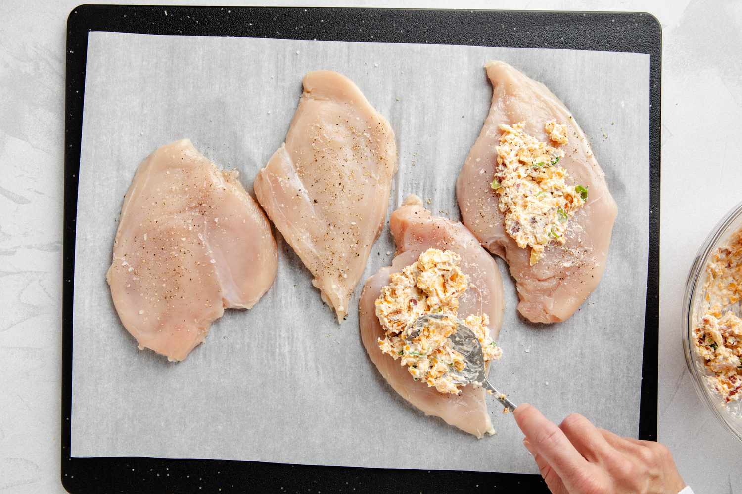 Million dollar dip spread onto flattened chicken breasts on a piece of parchment paper for million dollar chicken recipe