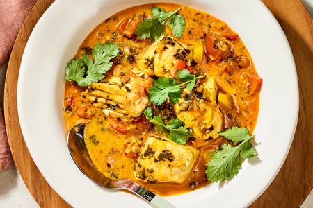 A bowl of moqueca Brazilian fish stew with fish pieces tomatoes herbs and broth garnished with cilantro