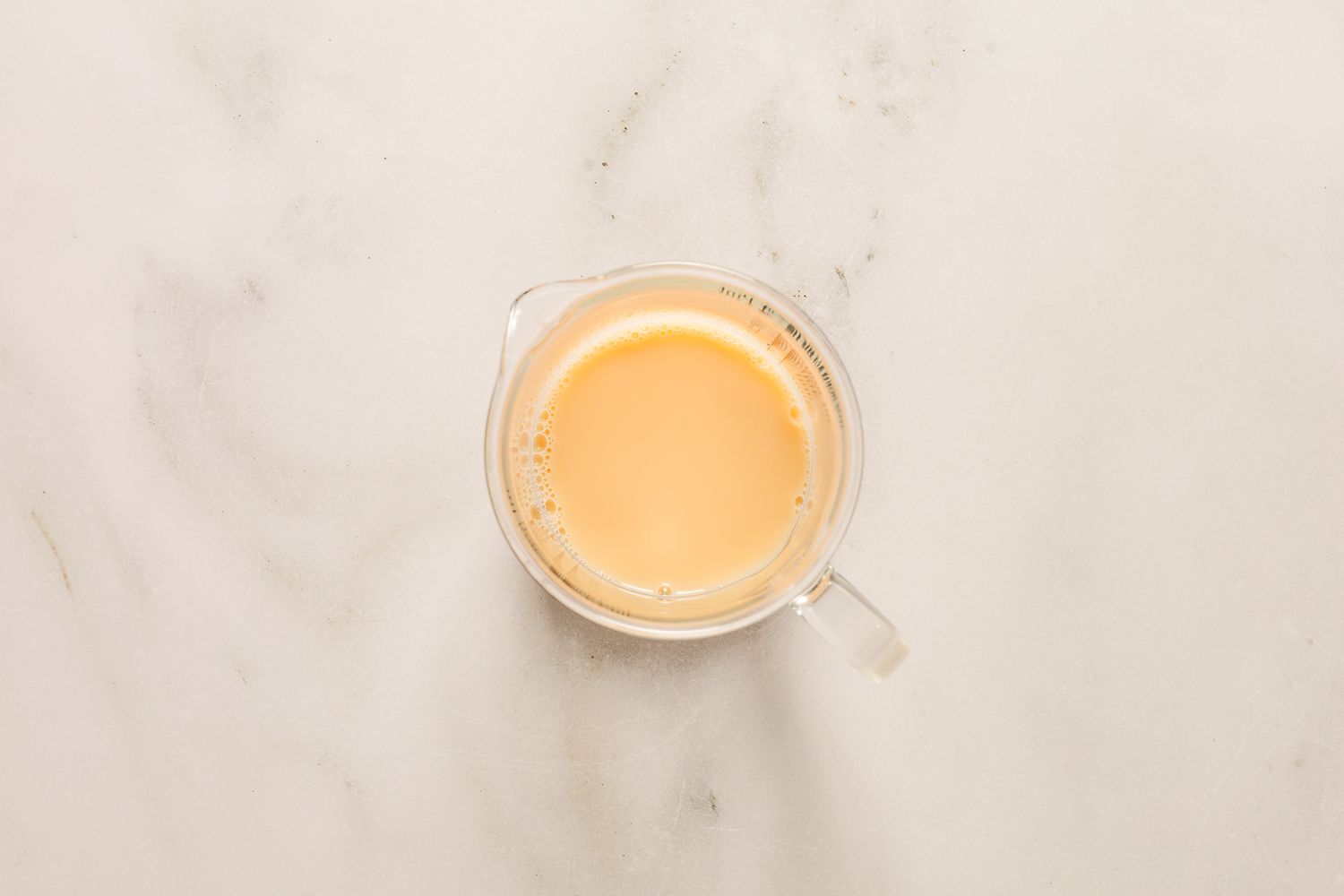 Overhead view of a clear glass measuring cup with egg yolk, cold water and vanilla extract mixed for Sand Tarts recipe