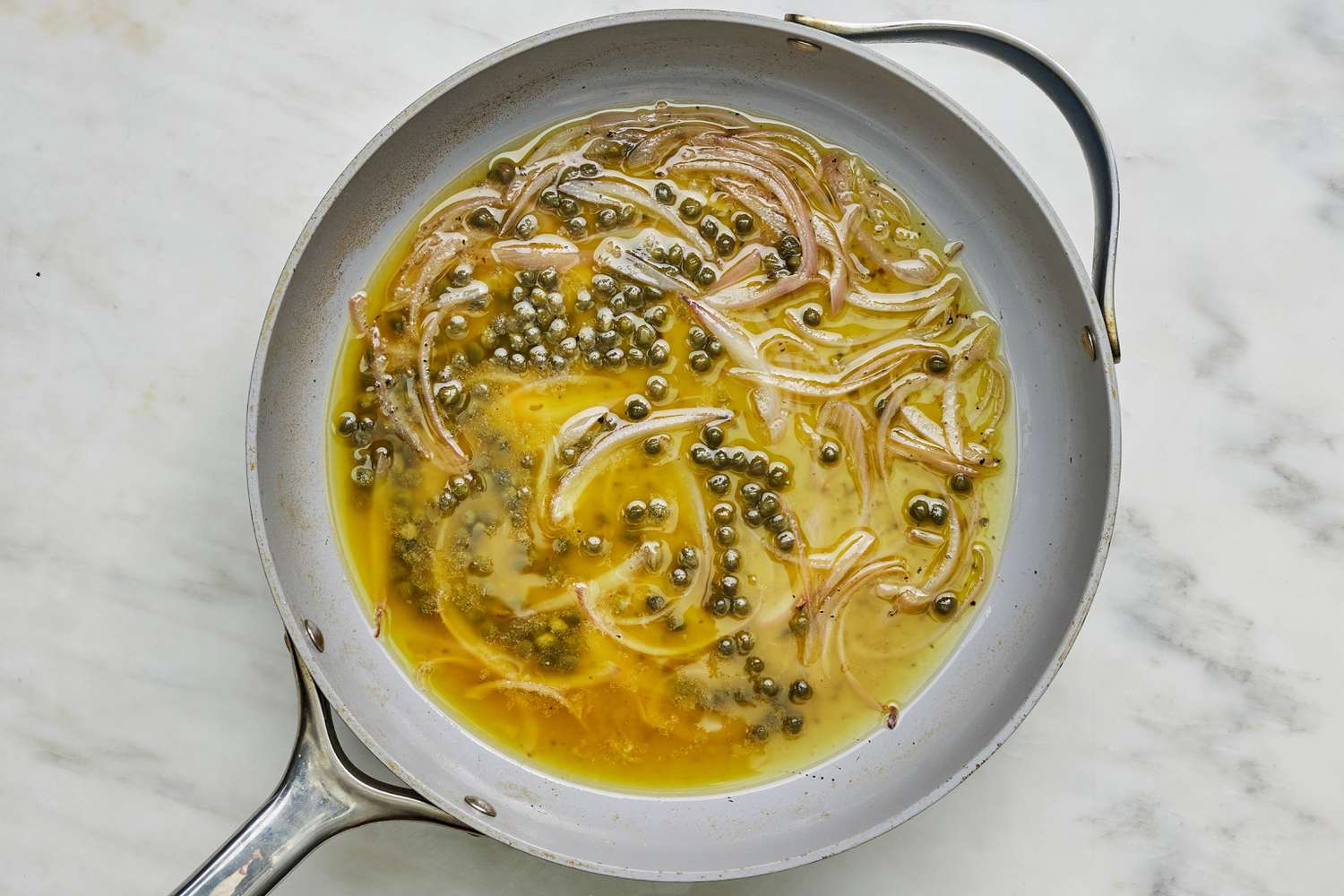 Onions and capers cooking in white wine mixture in a pan for 5-ingredient linguine with tuna and capers recipe