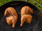 Two grilled half chickens on a barbecue grill