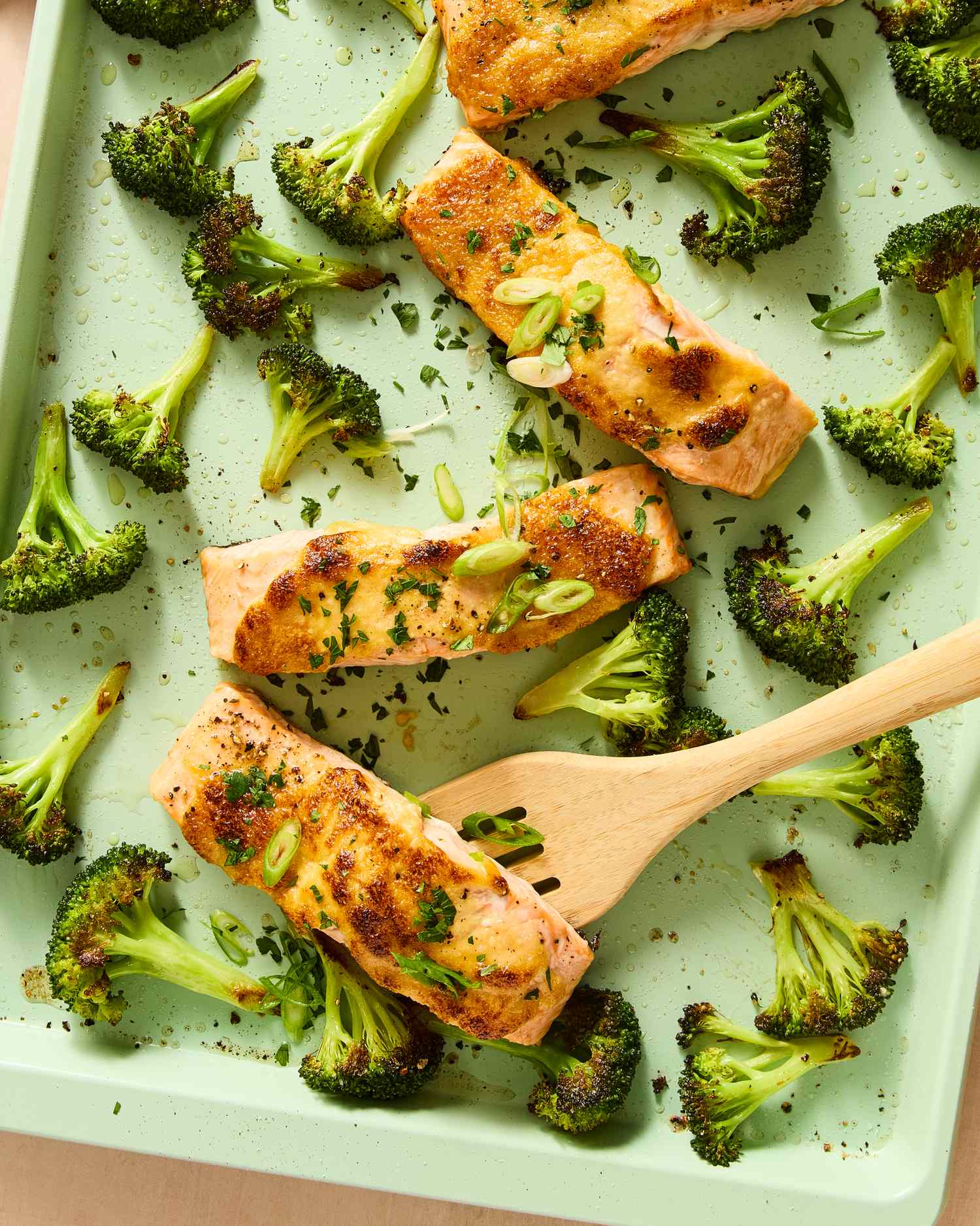 Salmon fillets and broccoli florets arranged on a sheet pan with a wooden serving utensil