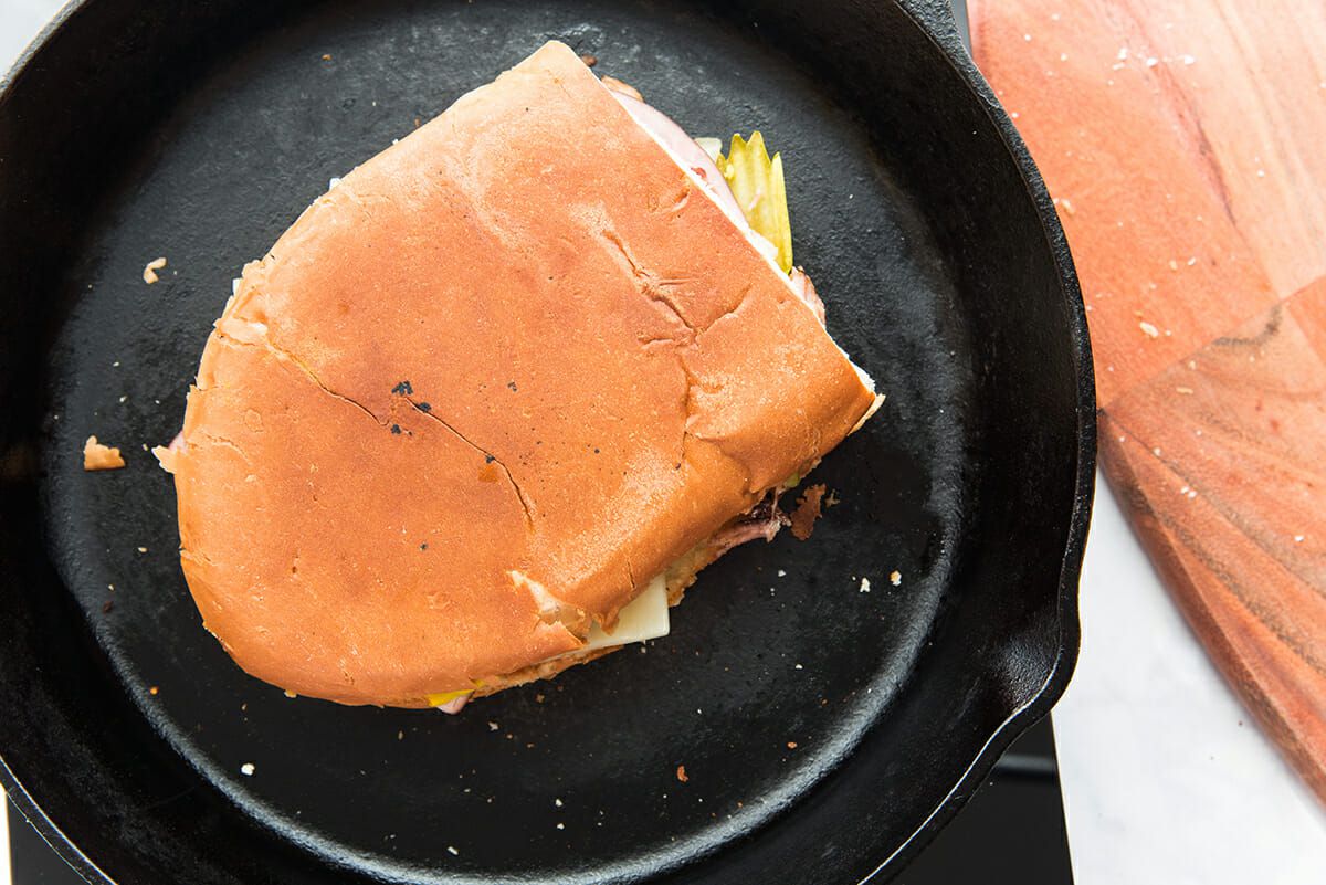 Pressed cuban sandwich set in a cast iron skillet. Pork, cheese and pickle peeking out the side.