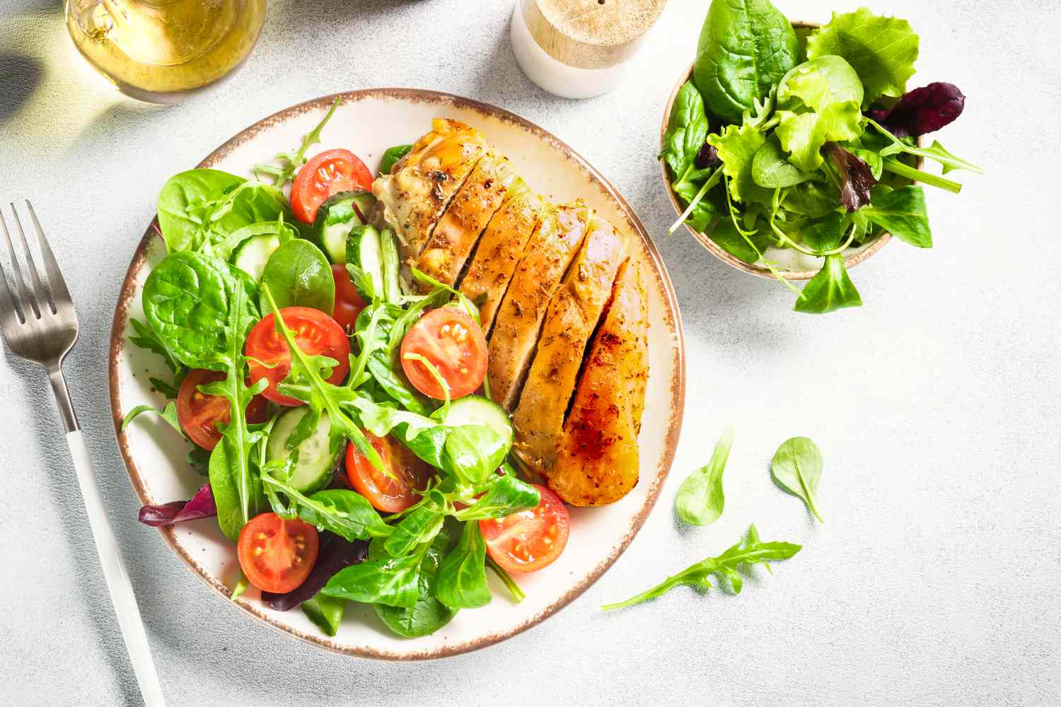 Overhead shot of sliced chicken breast next to a green side salad on a white plate