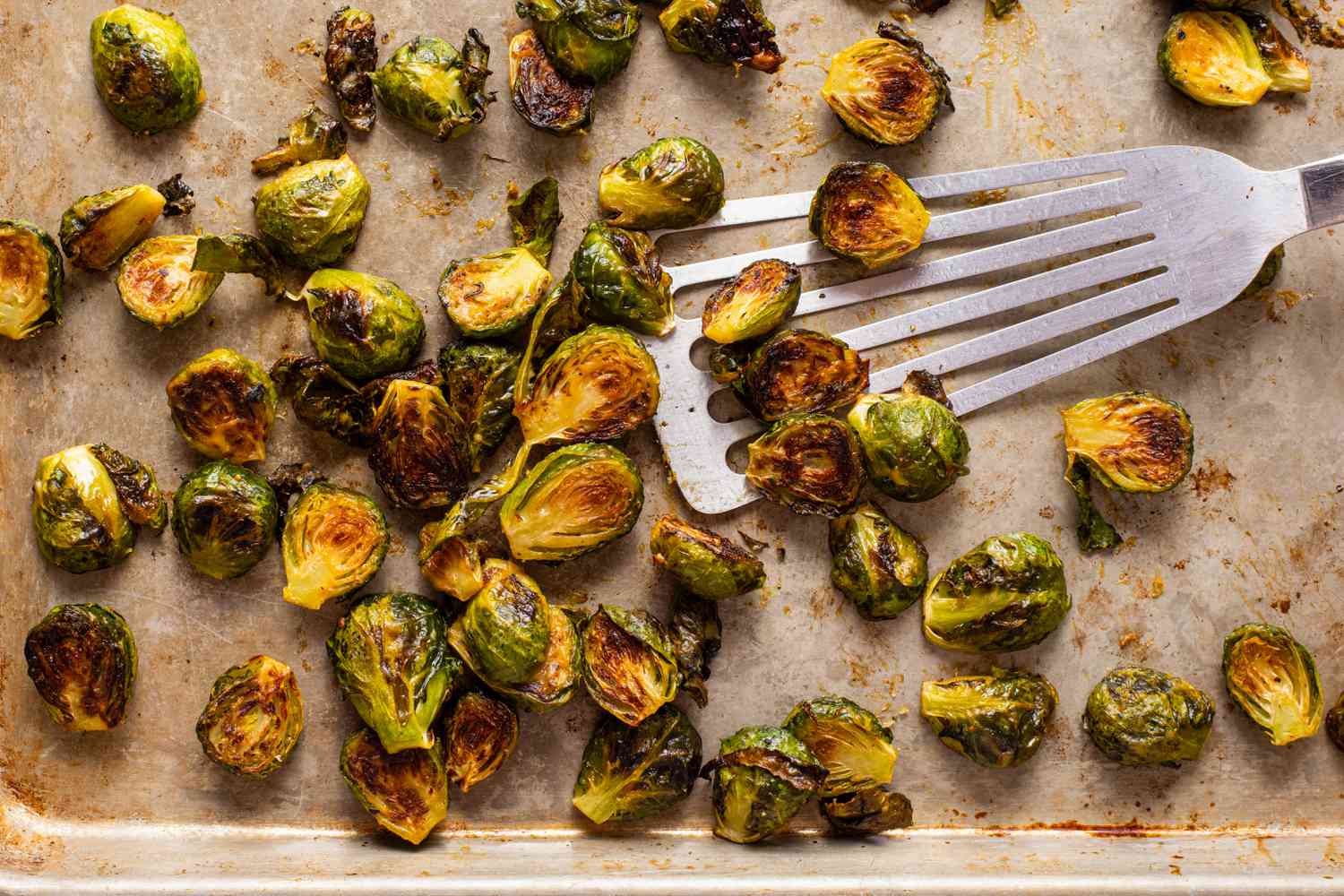 Honey mustard roasted Burssels sprouts on a baking sheet wuth a spatula