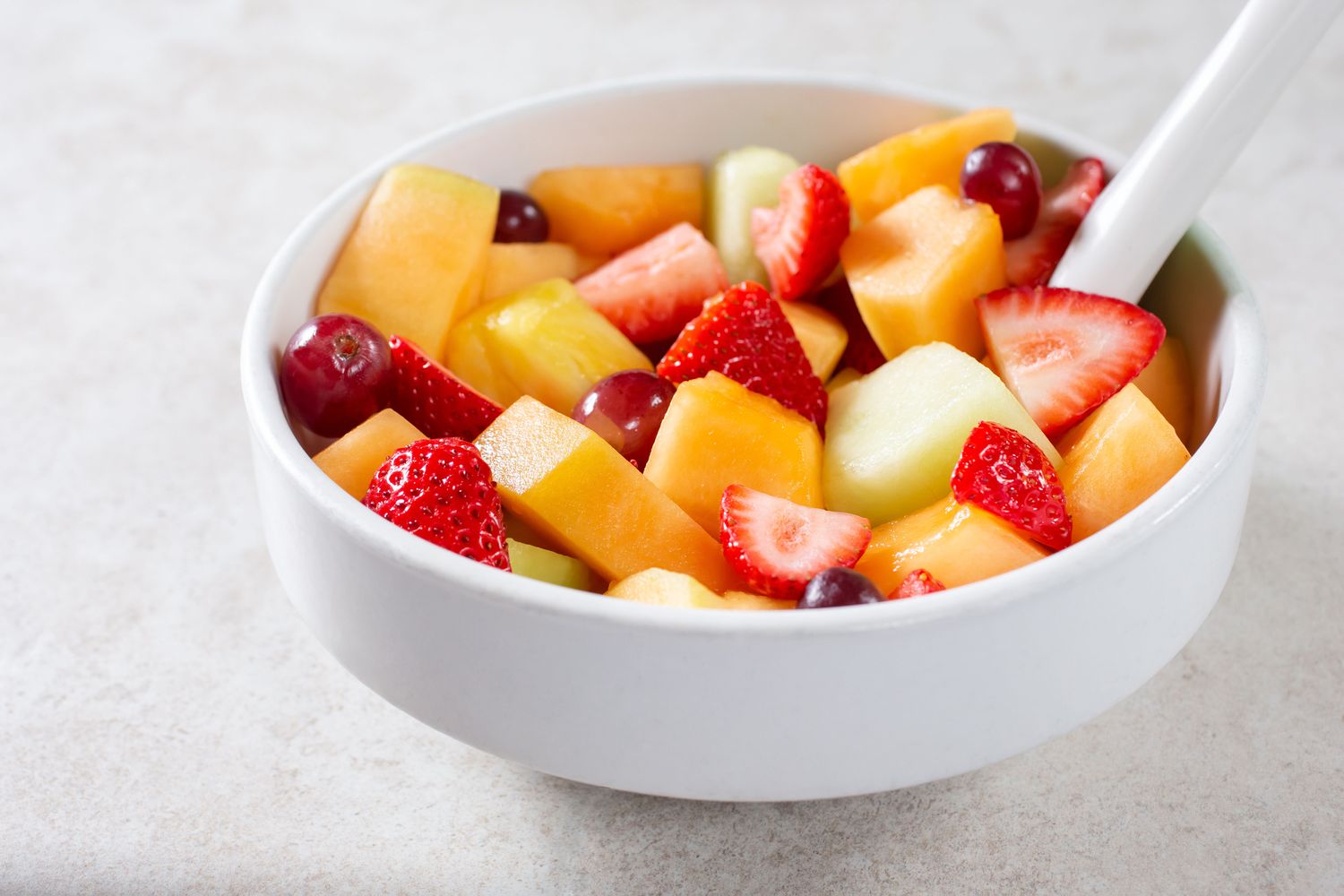 A bowl of fresh fruit salad containing melon, strawberries, grapes, and other fruit pieces