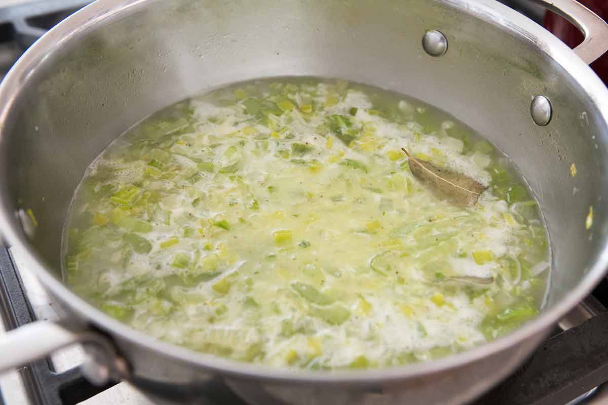 Celery and chicken stock cooking in a soup pot with a bay leaf 