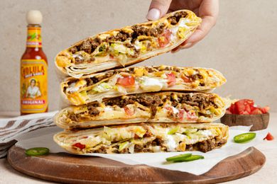 Hand Removing a Wrap from a Stack of Copycat Crunchwrap Supreme Wraps Cut in Half on Parchment Paper Over a Wooden Board