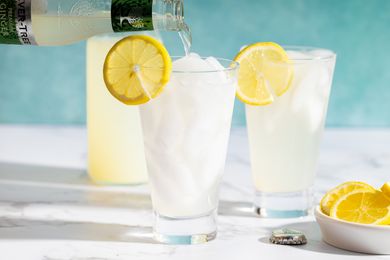Glasses of lemonade with lemon slices ice and a pouring beverage