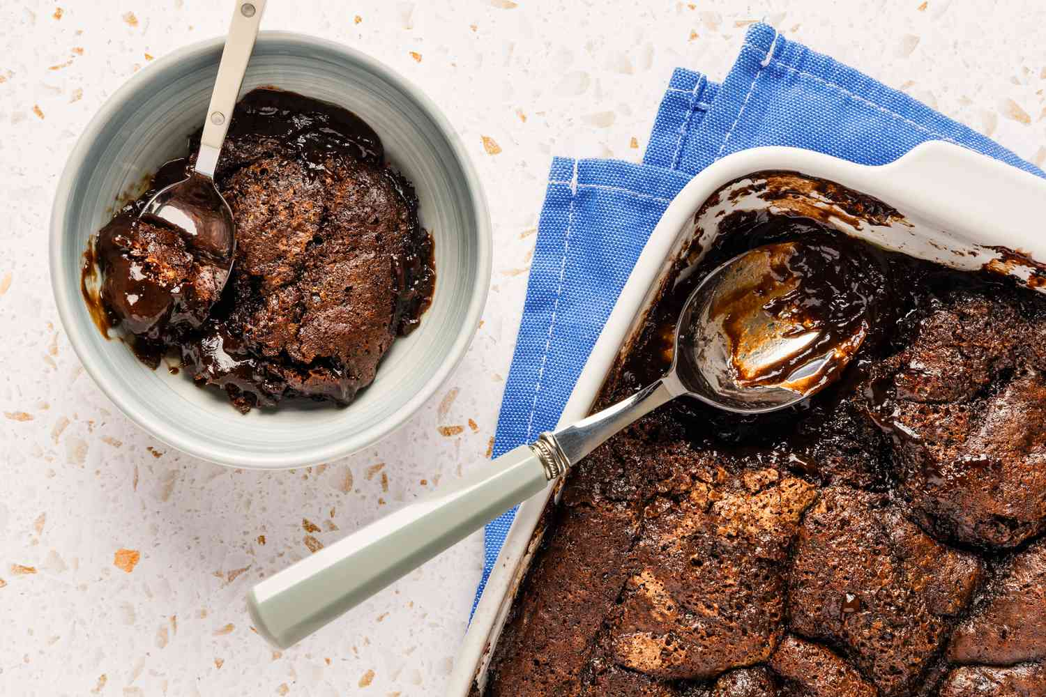 A bowl with a serving of chocolate cobbler, next to a baking pan with the rest of the cobbler