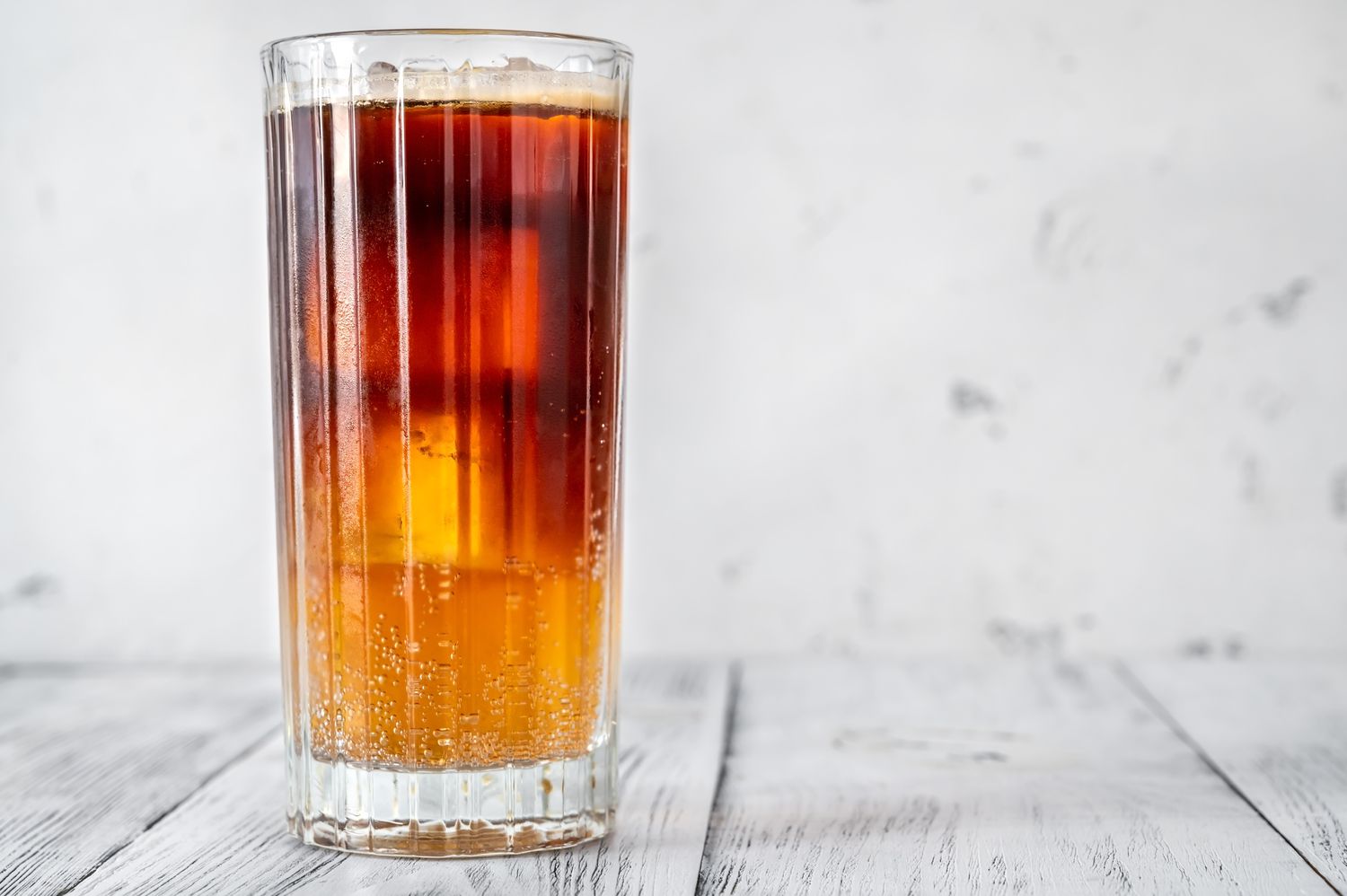 Iced coffee with seltzer in a tall glass, placed on a wooden surface.
