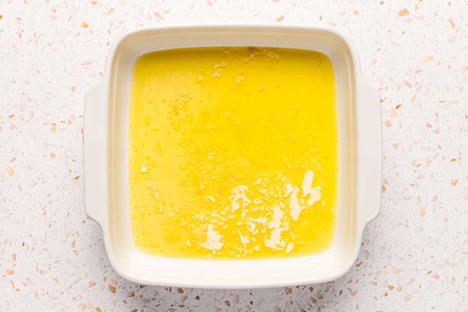Melted butter covering the bottom of a square baking dish for chocolate cobbler recipe
