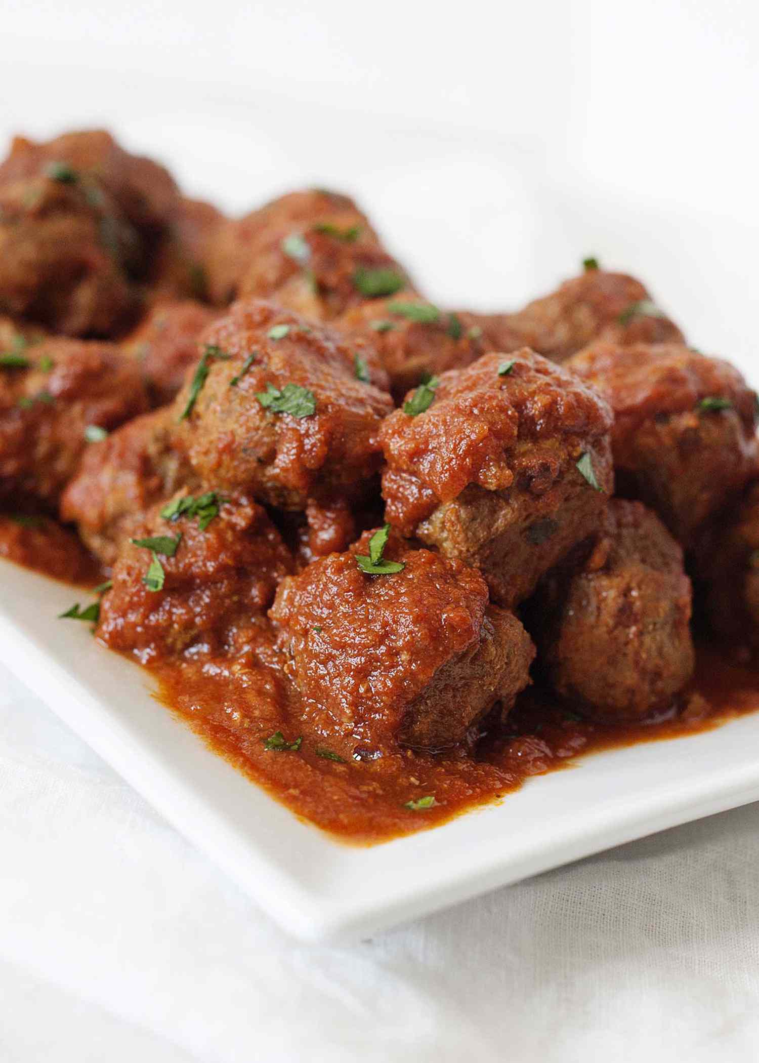Best Slow cooker italian meatballs in tomato sauce piled onto a white serving platter with a spoon.