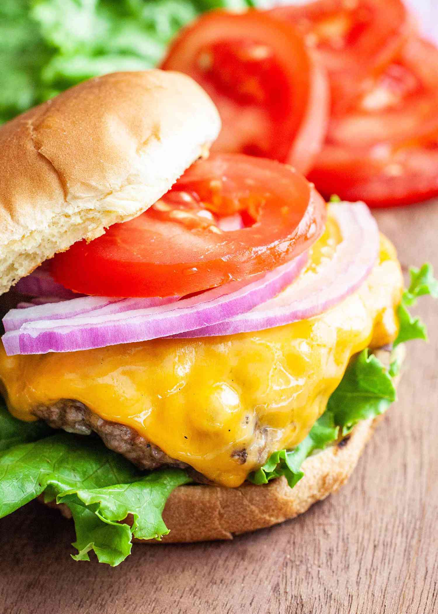 A burger topped with melty cheese, red onion, tomato, and lettuce
