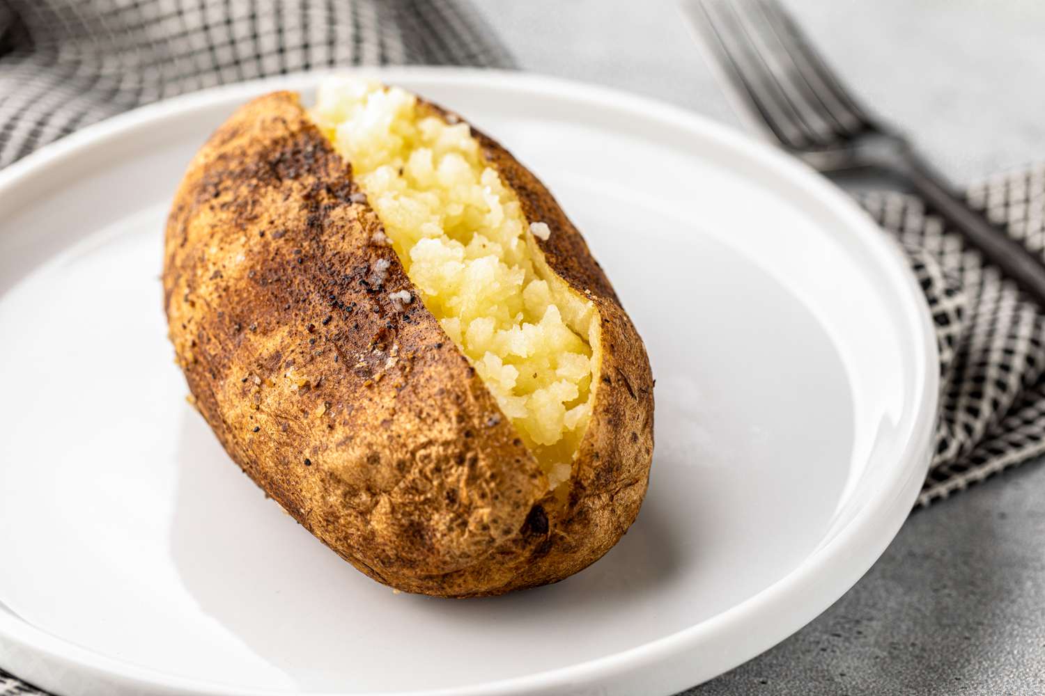 Opened Grilled Baked Potato on a Plate Next to a Fork and Napkin