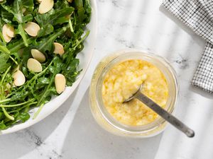 A glass jar with Whole Lemon Dressing next to a plate with a green arugula salad with chopped almonds