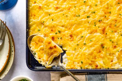 Overhead view of the corner of a sheet pan of Sheet Pan Au Gratin Potatoes recipe with a spoon scooping a serving out of the pan
