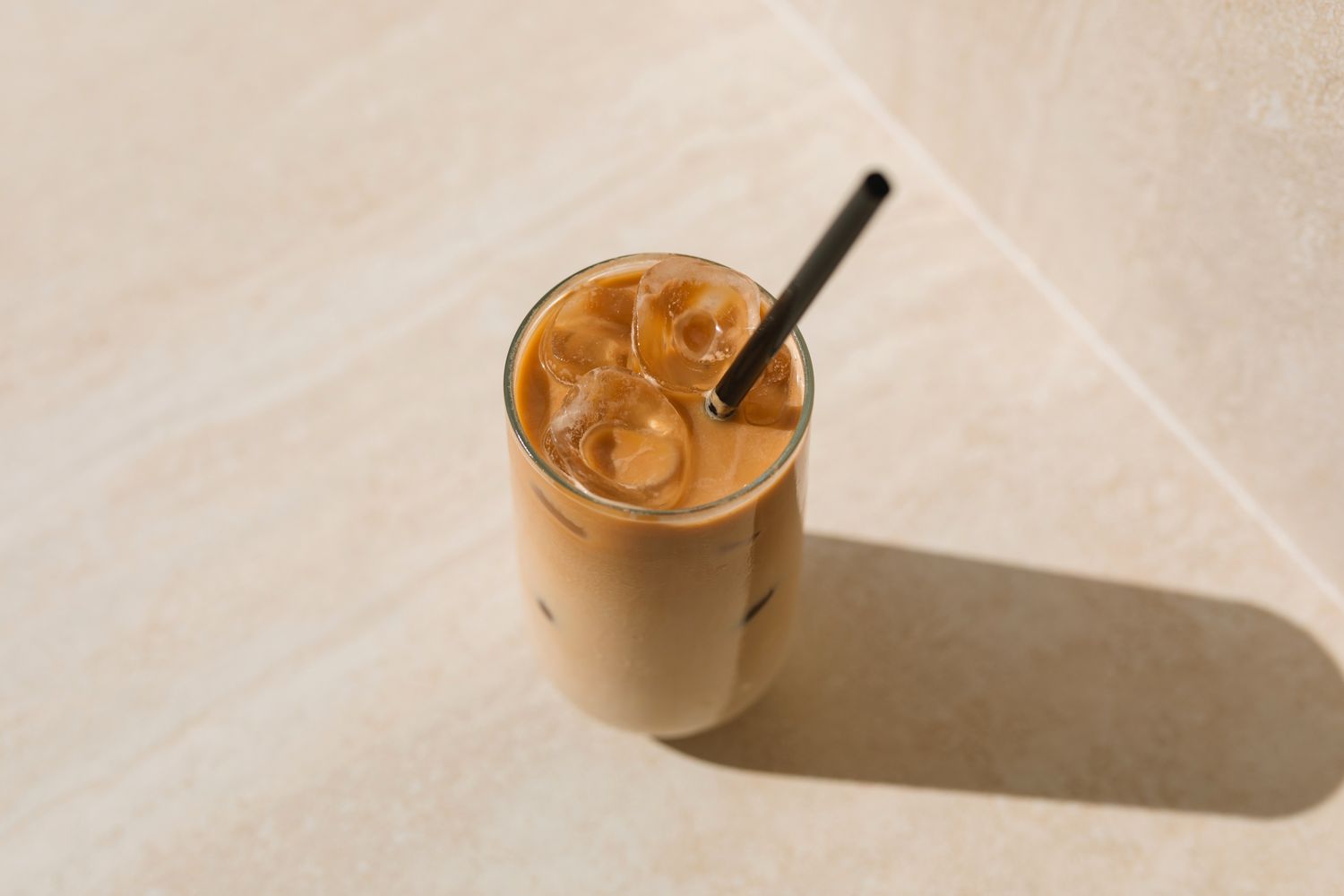 A glass of iced latte with a straw on a light surface