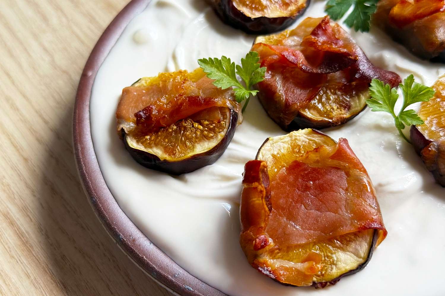 Slices of fig topped with prosciutto on a layer of cream with garnishes