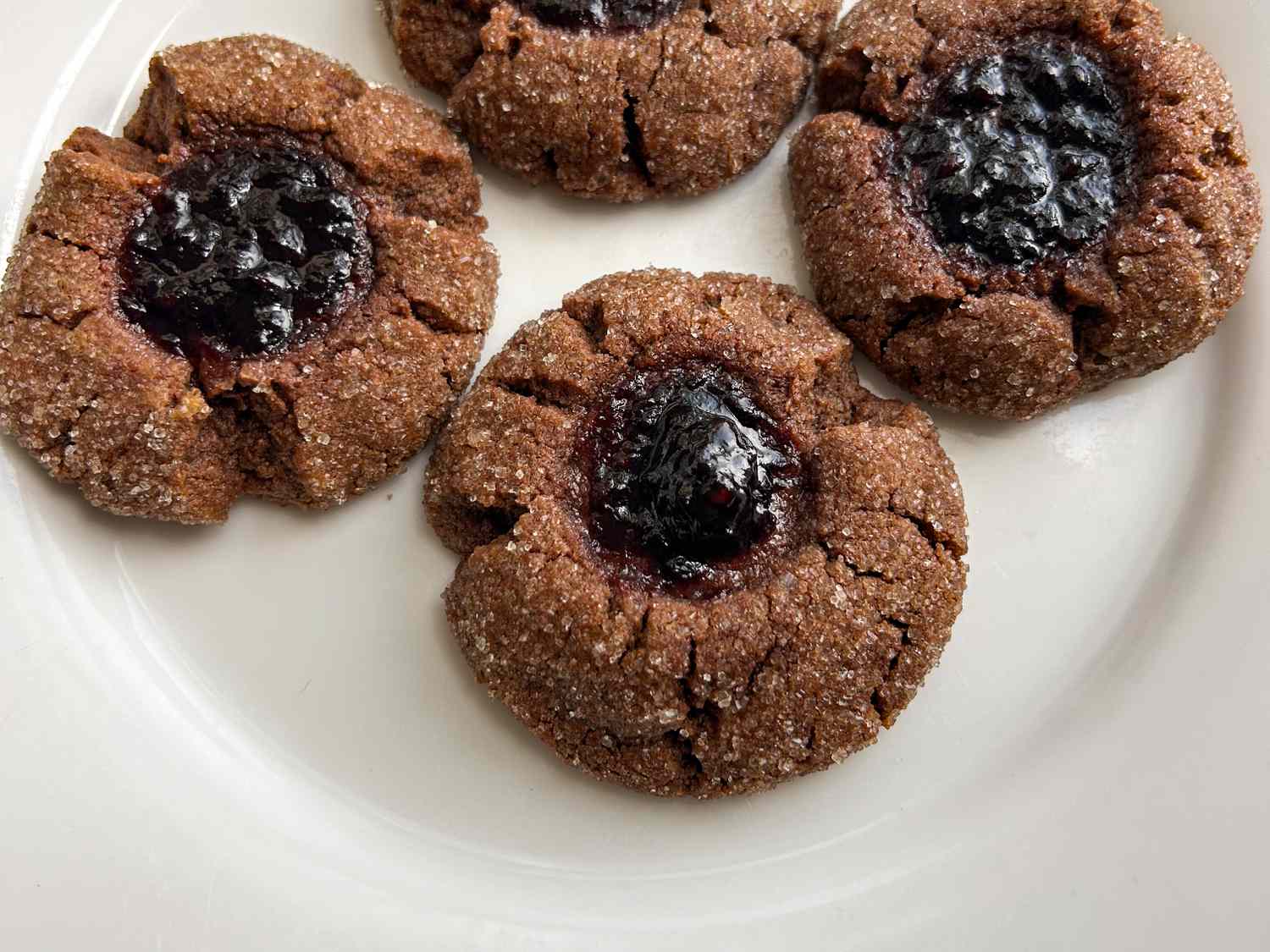 Four chocolate thumbprint cookies with a dark filling on a white plate