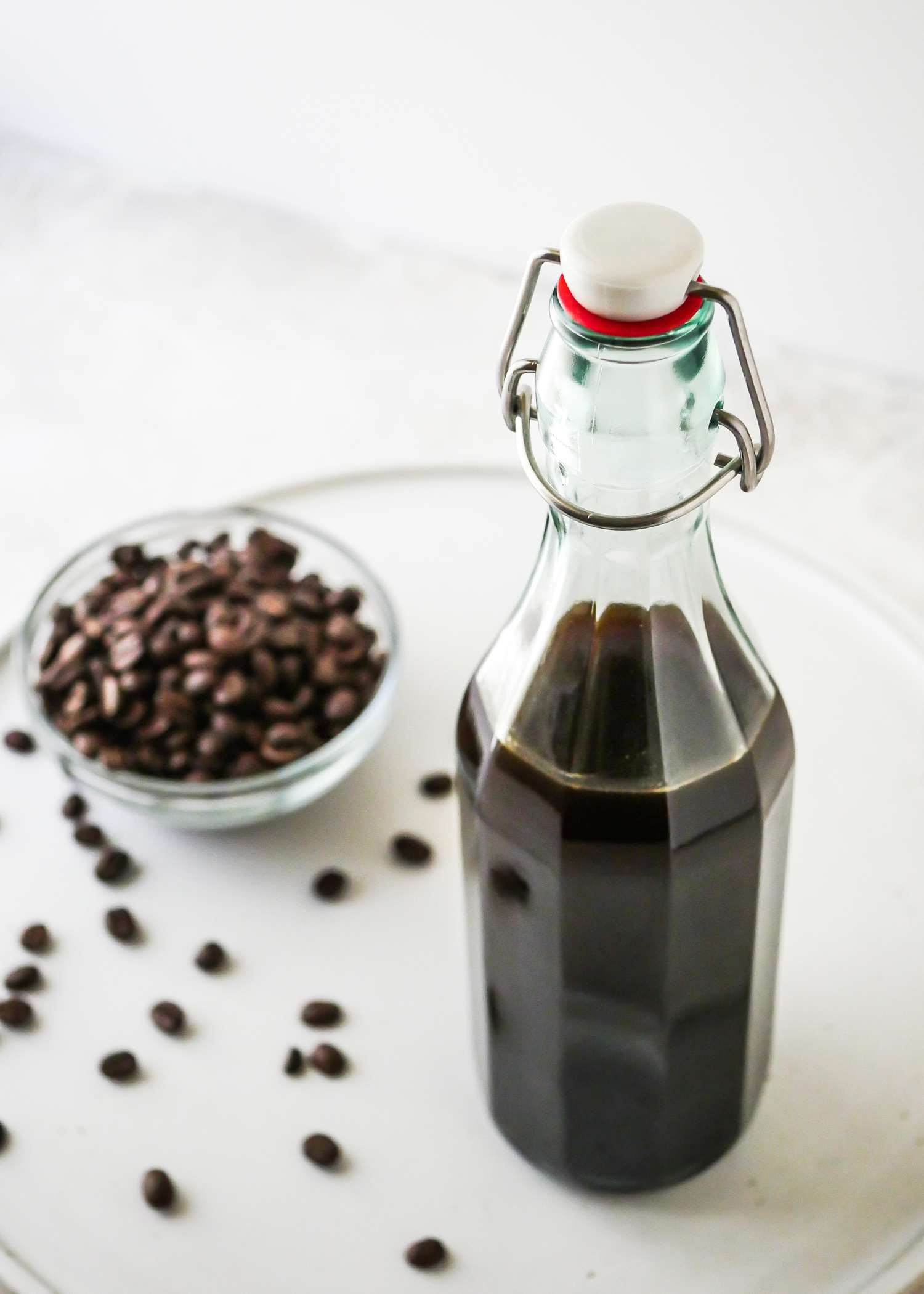 DIY Coffee Liqueur in a swing top bottle next to a small bowl of coffee beans.