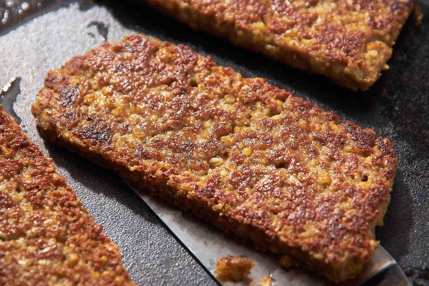 Sliced Goetta on a Griddle With a Spatula Slide Under One Piece 