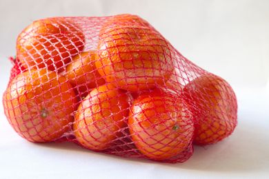 Oranges in a red mesh bag on a white background