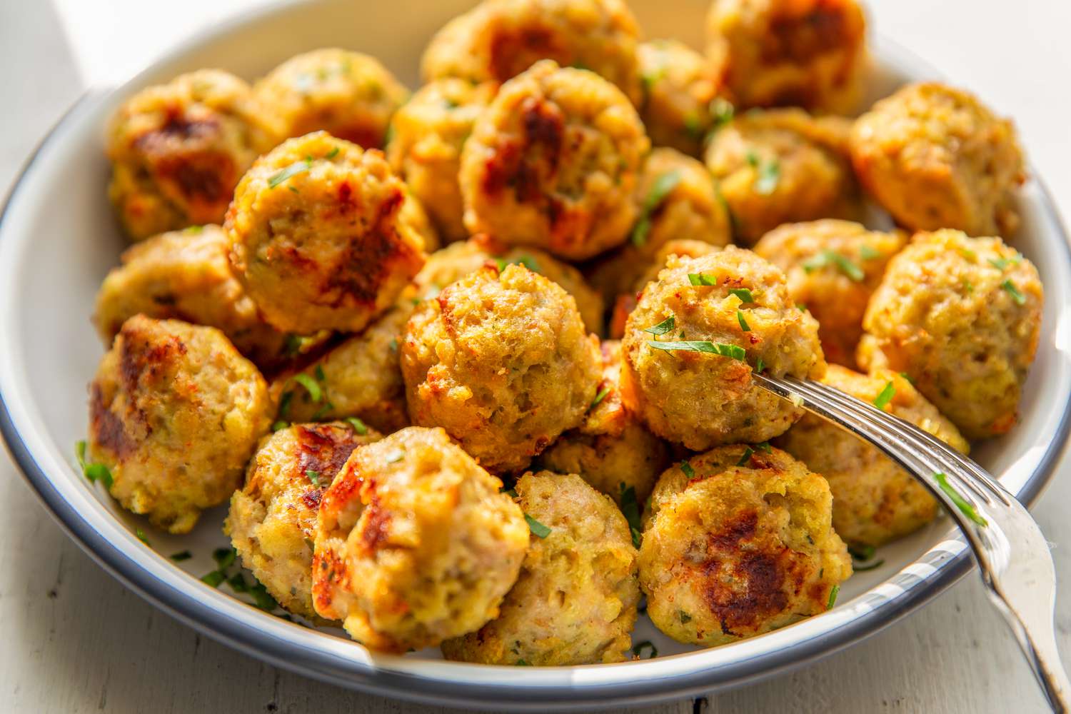 Closeup view of a bowl of 3-ingredient chicken meatballs with a fork on a white tabletop