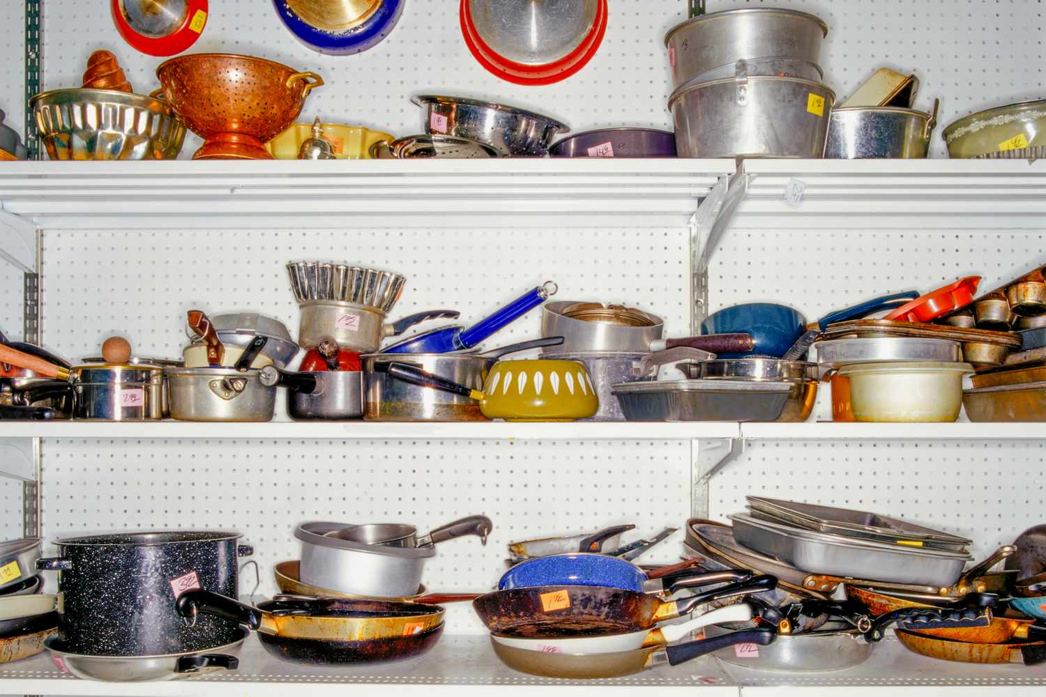 Shelves filled with assorted kitchen cookware and utensils in a thrift store setting