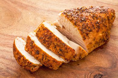 Moist and tender-looking spice-rubbed chicken breast partially sliced on a cutting board