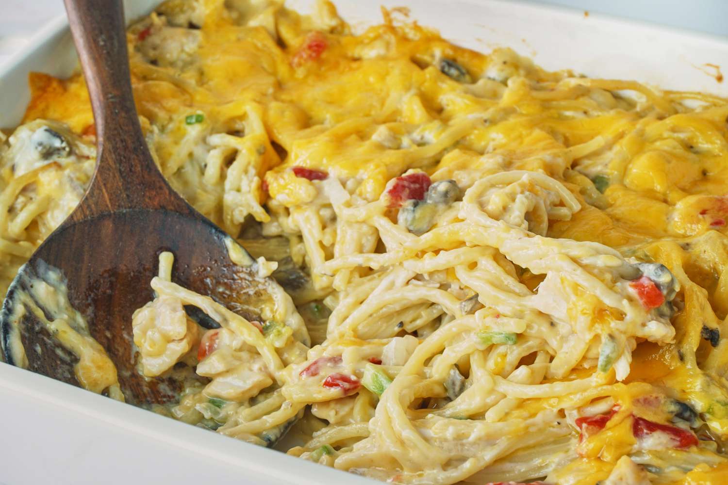 Ree Drummond's Chicken Spaghetti with cheese and vegetables wooden spoon in a casserole dish